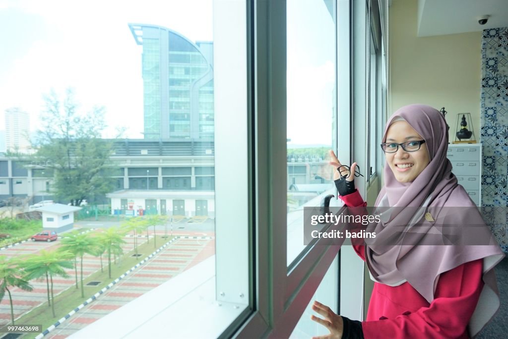 Beautiful young Muslimah students from Southeast Asian with hijab looking outside a windows library.