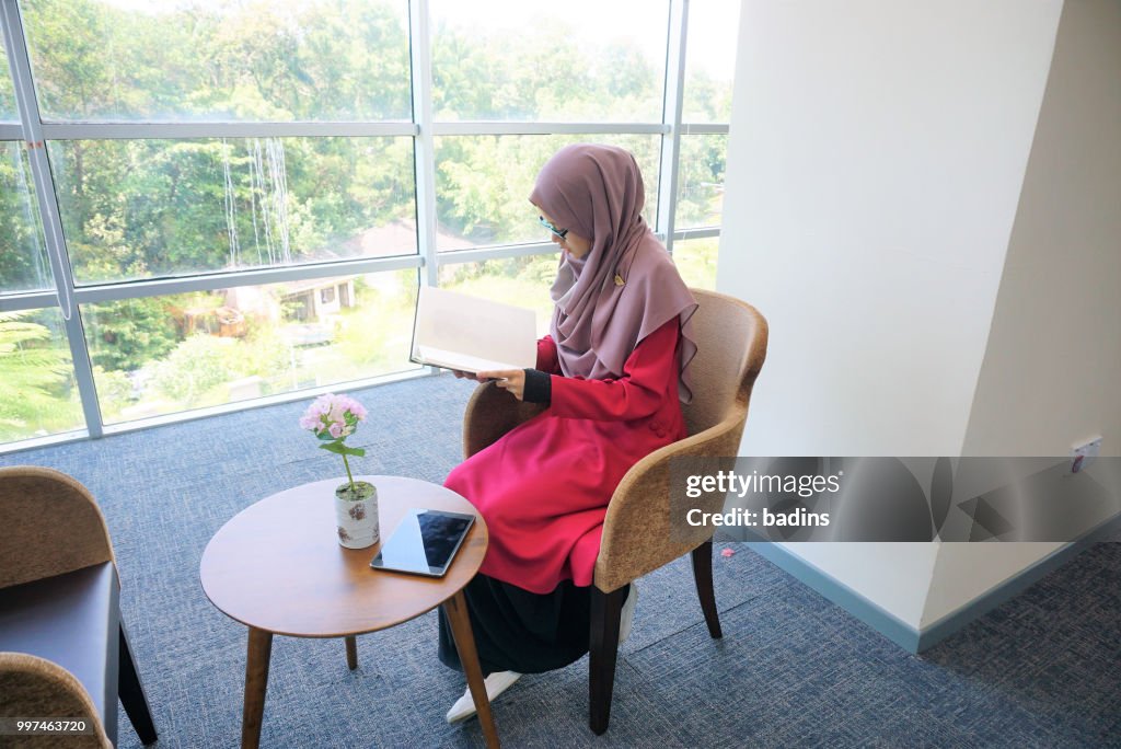 Beautiful young Muslimah students from Southeast Asian with hijab looking to the laptop and having discussion in the library.