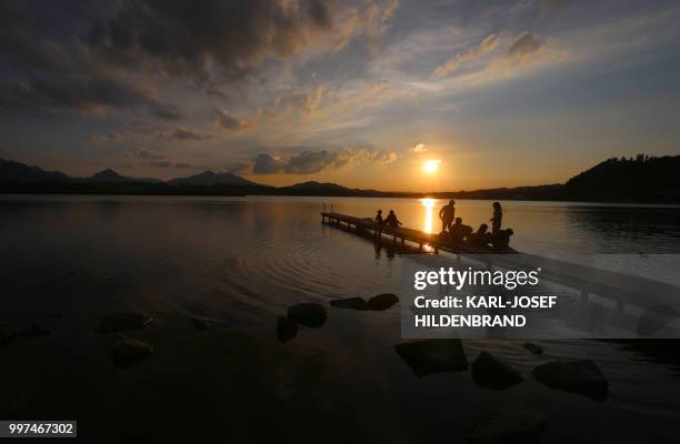 Picture taken on July 12, 2018 shows people enjoying the sunset on a wooden pier at the at the lake Hopfensee near Fuessen, southern Germany. - A...