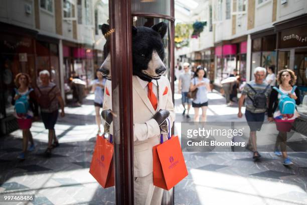 Shoppers pass a promotional bear model outside a luxury store as they walk through Burlington Arcade in central London, U.K., on Friday, Jun. 29,...