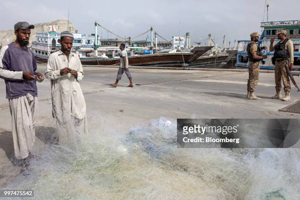 Fishermen tend to a fishing net as members of the security forces stand by at the harbor in Gwadar, Balochistan, Pakistan, on Tuesday, July 4, 2018....