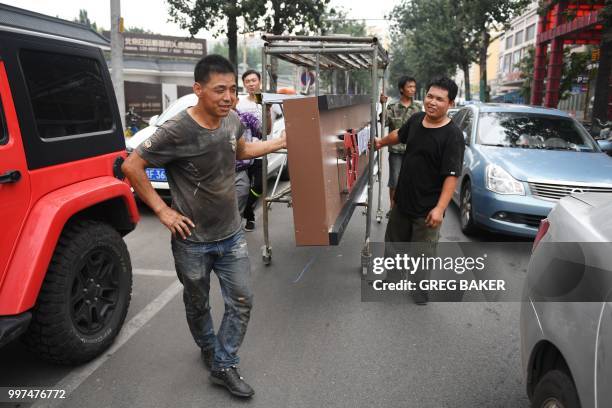 Workers haul a new sign for a supermarket along a street in Beijing on July 13, 2018. - China is expected to announce that the world's second-largest...