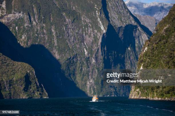 a boat cruises through the majestic cliffs of milord sound. - micah stock pictures, royalty-free photos & images