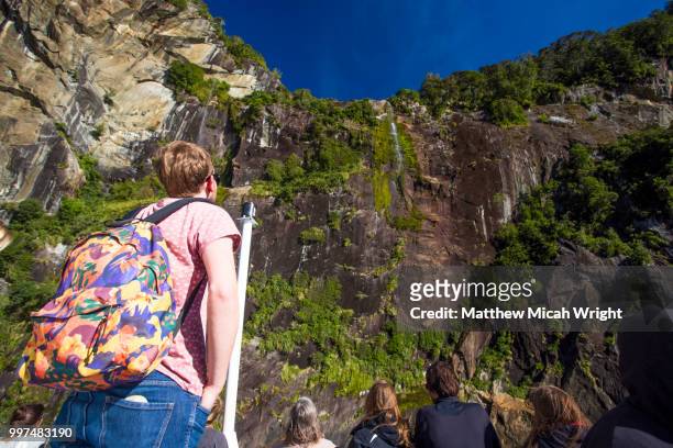 a traveler gazes at the towering mountainous walls surrounding him in milford sound. - micah stock pictures, royalty-free photos & images