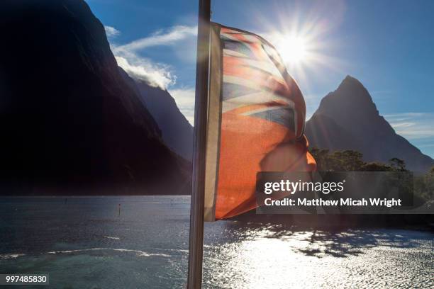 milford sound national park with the iconic mitre peak in the background along with the new zealand flag. - pico mitre fotografías e imágenes de stock