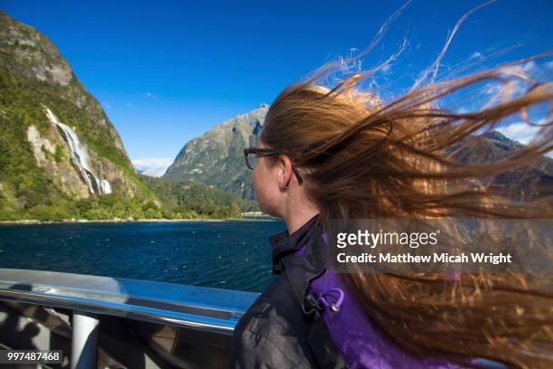 a girl glances watches the beautiful scenery pass by on the way through milford sound on a boat. her hair blows in the wind. - micah stock pictures, royalty-free photos & images