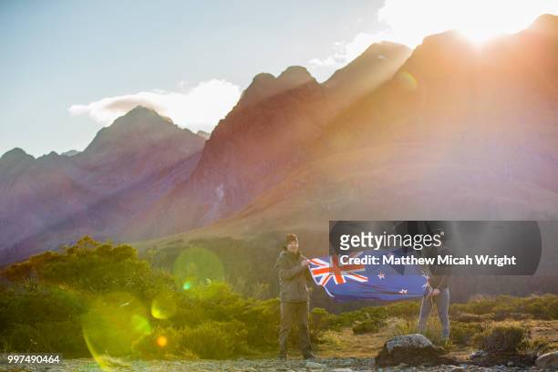 a hike through the key summit track as part of the routeburn track in the fiordland national park. people pose with the new zealand national flag. - micah stock pictures, royalty-free photos & images