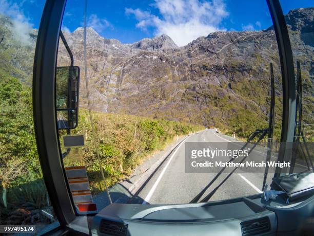 a bus passes through the mountain passes and towering mountains of the milford sound national park. - micah stock pictures, royalty-free photos & images