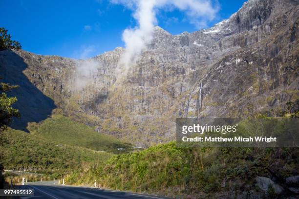 a road through the mountain passes and towering mountains of the milford sound national park. in the distance you can see the dwarfed homer tunnel which provides the only road passage in and out. - micah stock pictures, royalty-free photos & images