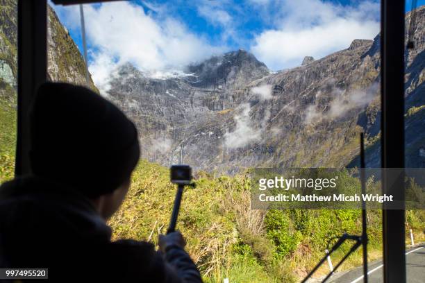 a person photographs out of a bus window as it passes through the mountain passes and towering mountains of the milford sound national park. - micah stock pictures, royalty-free photos & images