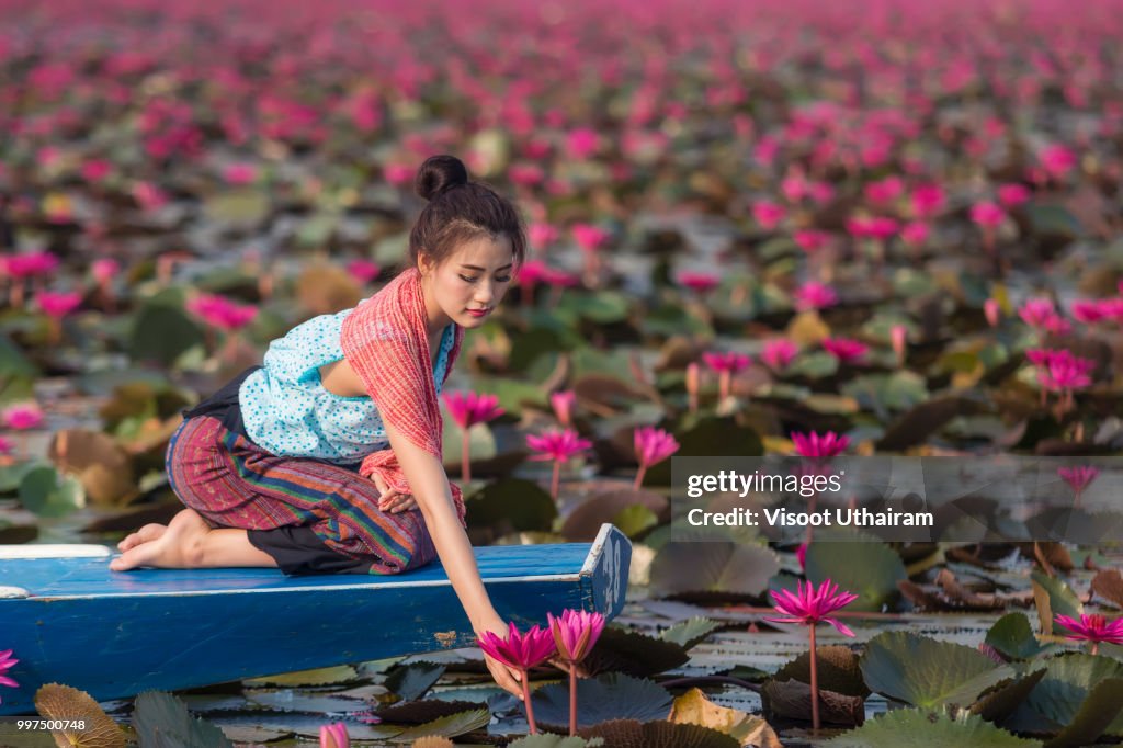 Beautiful Thai lady in Thai dress sitting on boat is holding lotus in the river.