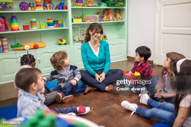 leraar vertellen van een verhaal voor kinderen in de kleuterschool - small child sitting on floor stockfoto's en -beelden