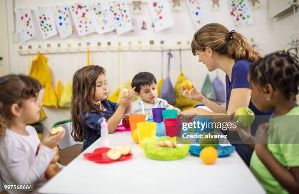 lehrer, die früchte, schüler im klassenzimmer zu erklären - kindergartengebäude stock-fotos und bilder