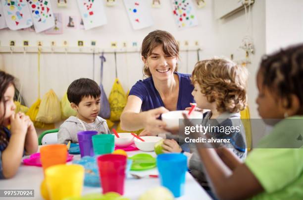 leraar met preschool kinderen op bureau tijdens de lunch - peuterschool gebouw stockfoto's en -beelden