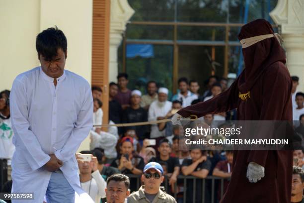 Graphic content / A member of Indonesia's Sharia police whips a man accused of having gay sex during a public caning ceremony outside a mosque in...