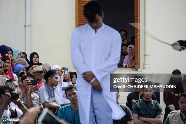Graphic content / TOPSHOT - Onlookers watch as a member of Indonesia's Sharia police whips a man accused of having gay sex during a public caning...