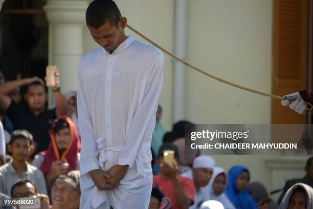 Graphic content / A member of Indonesia's Sharia police whips a man accused of having gay sex during a public caning ceremony outside a mosque in...