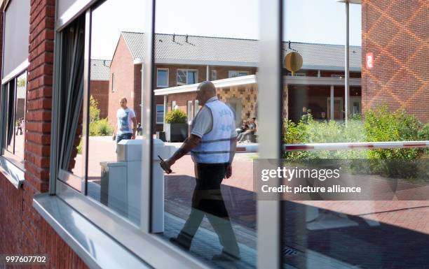 July 2018, Netherlands, Ter Apel: A guard with a waltie-talkie in his hand reflected in a window at the entrance to the central reception centre for...