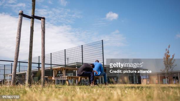 July 2018, Netherlands, Ter Apel: Two men sitting on a bench at the central reception centre for asylum seekers 'VluchtelingenWerk Noord-Nederland...
