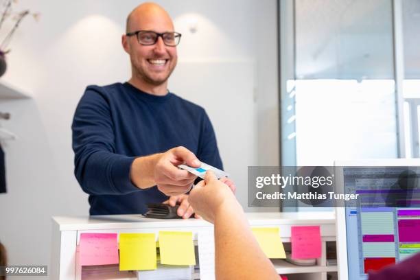 at the reception of a surgery a patient handing over his health card - empfang stock-fotos und bilder