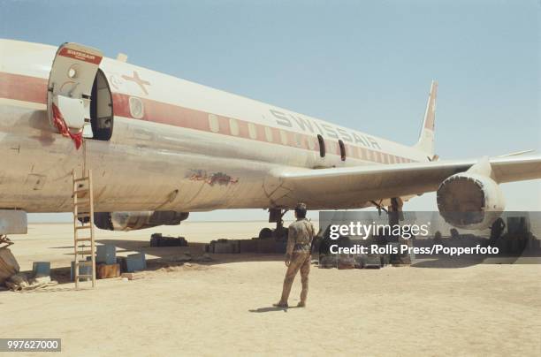 View of an armed guard standing in front of a Swissair Douglas DC-8 on Flight 100 parked on the ground at Dawson's Field airstrip in Jordan after...