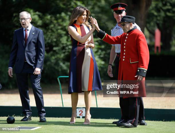 First Lady Melania Trump high-fives with a British military veteran known as a "Chelsea Pensioner" during a game of bowls with Philip May, the...