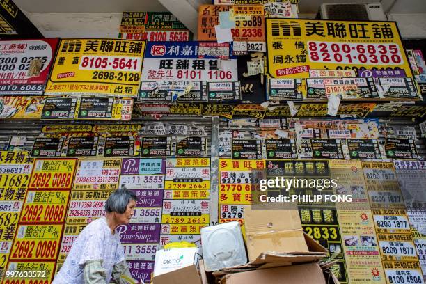 Woman pushes a cart with cardboard in front of a vacant shop with posters of rental advertisements in the Kowloon district of Hong Kong on July 13,...