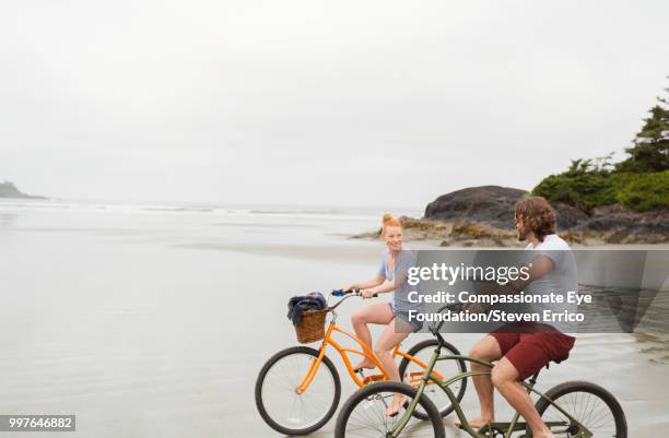 smiling couple bike riding on beach - dark haired man gray shirt with wine stock pictures, royalty-free photos & images