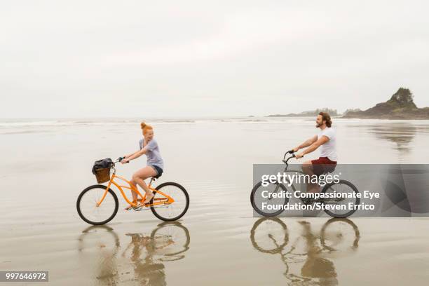smiling couple bike riding on beach - barefoot redhead ストックフォトと画像