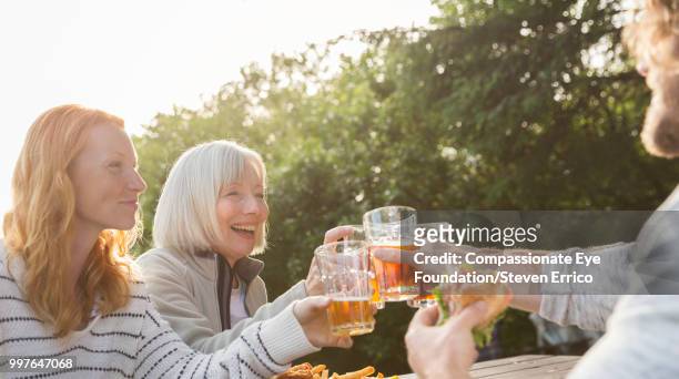 senior woman and family toasting with beer glasses at campsite picnic table - senior man grey long hair stock pictures, royalty-free photos & images