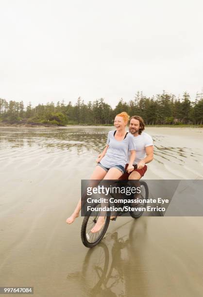 playful couple bike riding on beach - handlebar stock pictures, royalty-free photos & images
