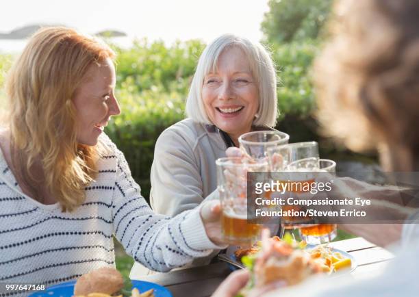 senior woman and family toasting with beer glasses at campsite picnic table - sogra imagens e fotografias de stock