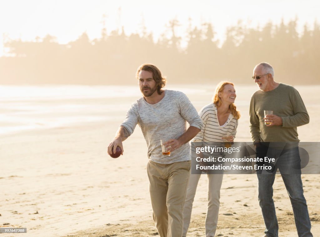 Smiling senior man and family playing boules on beach at sunset