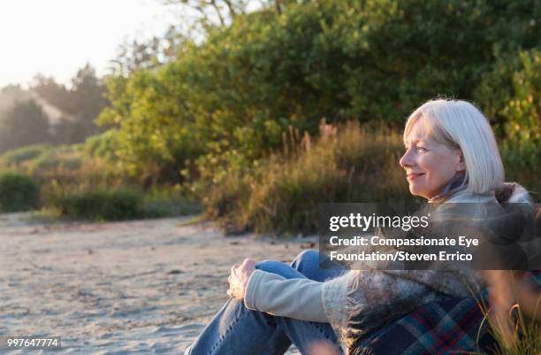 senior woman sitting on beach at sunset - eskapismus stock-fotos und bilder