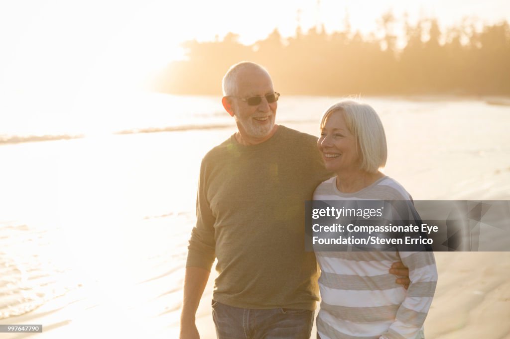 Smiling senior couple walking on beach at sunset