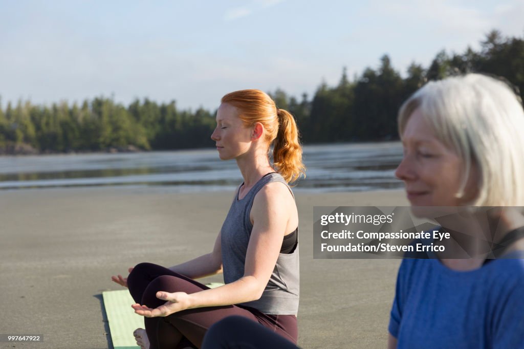 Senior woman and daughter practicing yoga on beach