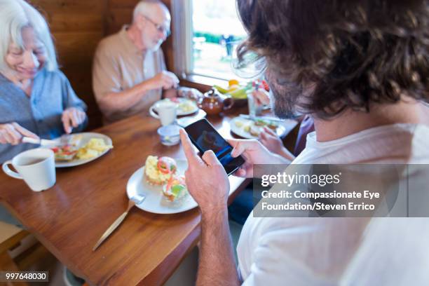 man using cell phone at breakfast with family in cabin - technophiler mensch stock-fotos und bilder