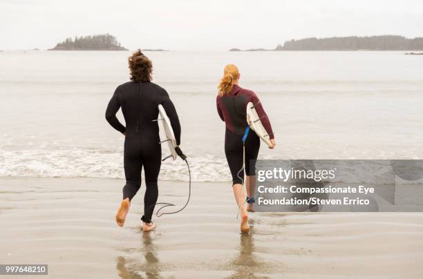 surfers running into waves with surfboards - compassionate eye foundation stockfoto's en -beelden