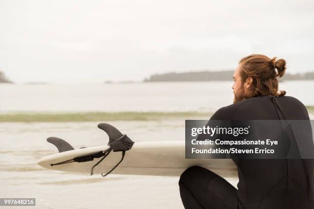 surfer holding board looking at ocean view - "compassionate eye" fotografías e imágenes de stock