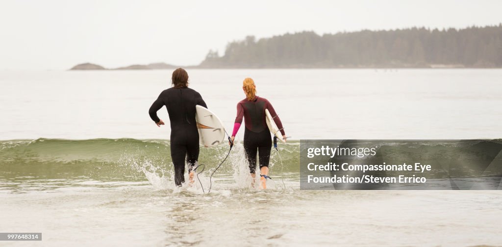 Surfers running into waves with surfboards