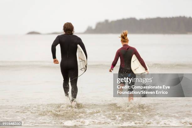 surfers running into waves with surfboards - "compassionate eye" fotografías e imágenes de stock