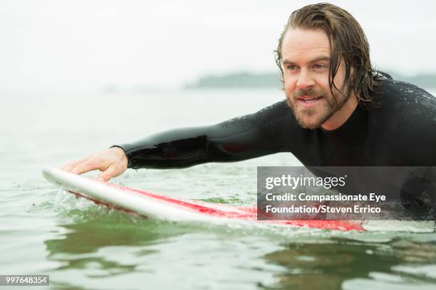 surfer paddling on surfboard in sea - "compassionate eye" fotografías e imágenes de stock