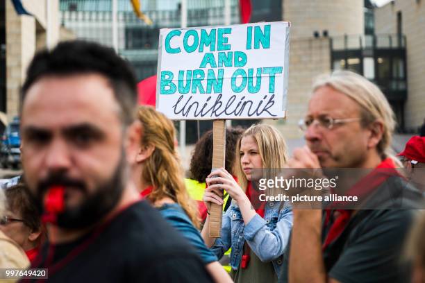 July 2018, Germany, Dusseldorf: Striking staff members of the university hospital holding a sign with the words 'Come in and burn out'. Around 500...