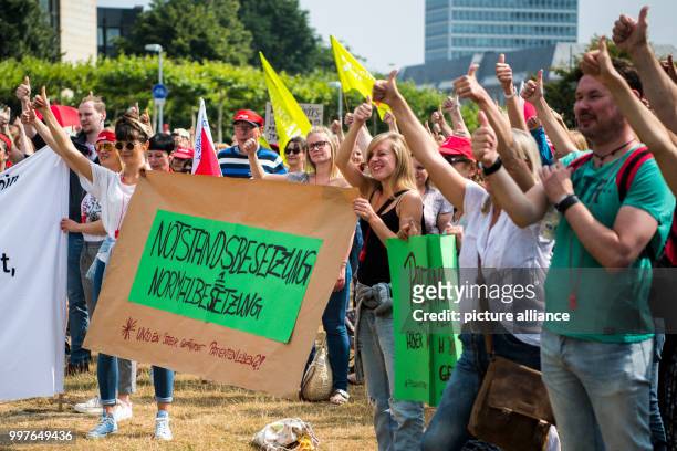 July 2018, Germany, Dusseldorf: Striking staff members of the university hospital holding a sign with the words 'Notstandsbesetzung =...