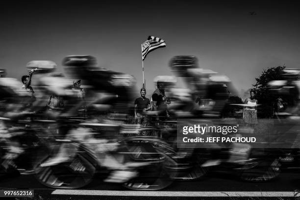 Spectator waves the flag of Brittany as riders speed following their first ascend of the Mur-de-Bretagne hill during the sixth stage of the 105th...
