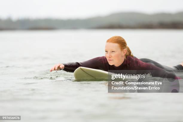 female surfer paddling on surfboard in sea - "compassionate eye" fotografías e imágenes de stock