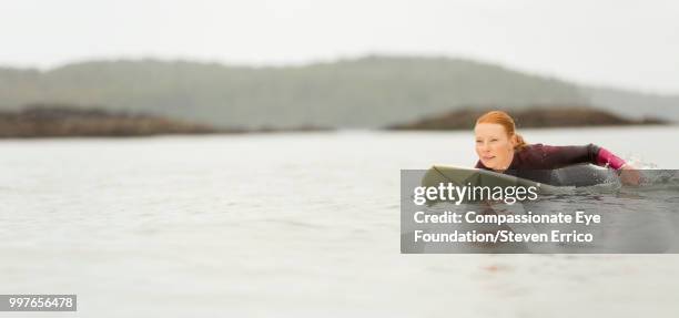 female surfer paddling on surfboard in sea - compassionate eye stockfoto's en -beelden