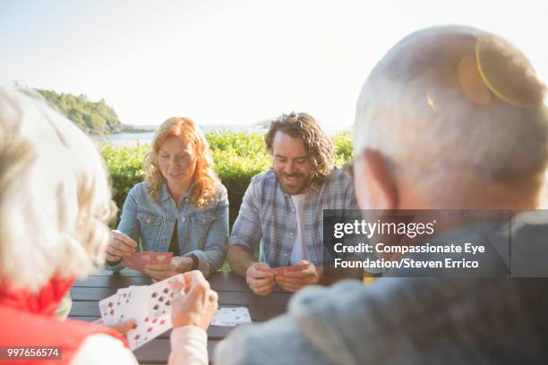 senior couple and adult children playing cards at campsite picnic table - senior man grey long hair stock pictures, royalty-free photos & images