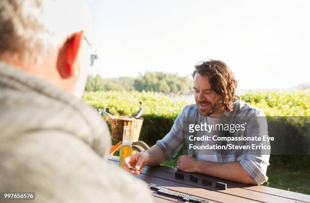 senior man and adult son playing dominoes at campsite picnic table - camping games stockfoto's en -beelden