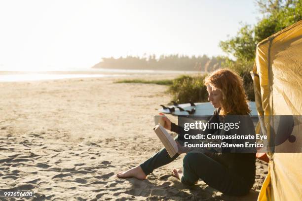 woman reading book on beach - eskapismus stock-fotos und bilder